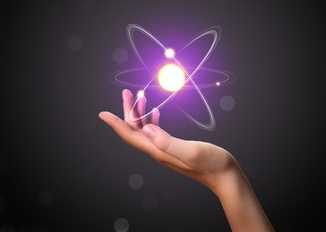 Woman and virtual model of atom on dark background, closeup
