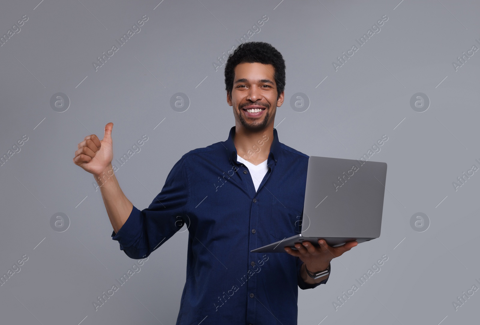 Photo of Happy man with laptop showing thumb up on grey background