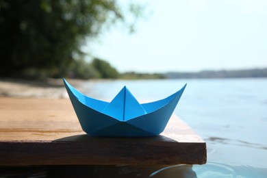 Photo of Light blue paper boat on wooden pier near river