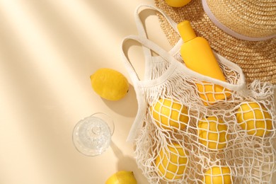 Photo of Fresh lemons, beach accessories in string bag and glass of drink on beige background, flat lay. Space for text
