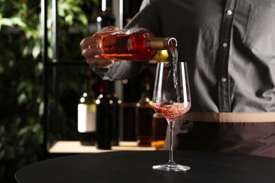 Photo of Man pouring rose wine from bottle into glass indoors, closeup
