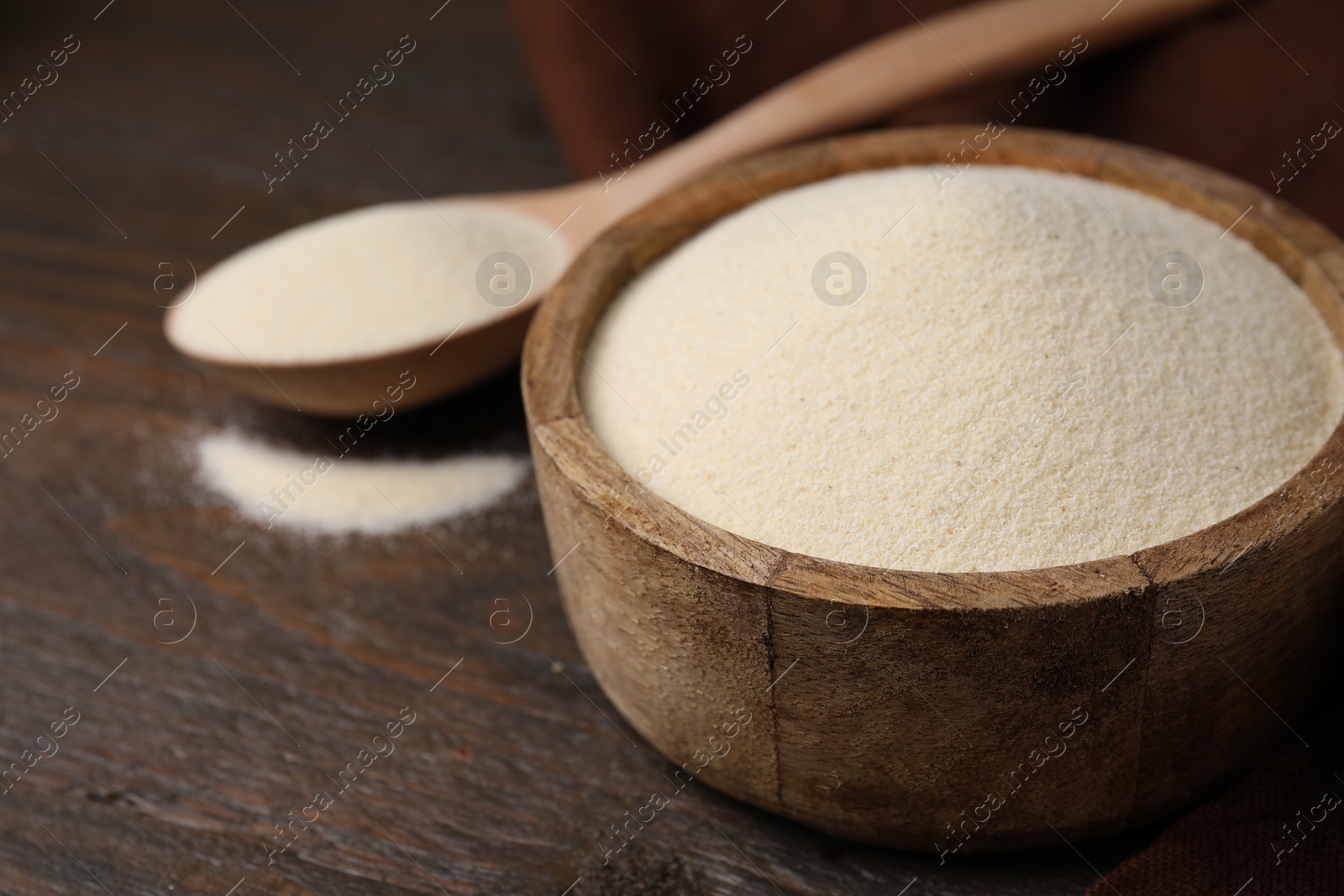 Photo of Uncooked organic semolina in bowl and spoon on wooden table, closeup. Space for text