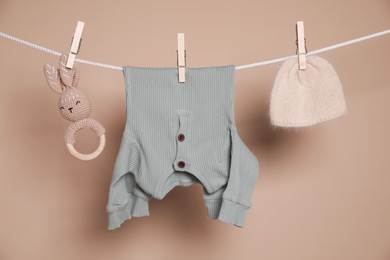 Photo of Cute small baby clothes and toy hanging on washing line against brown background