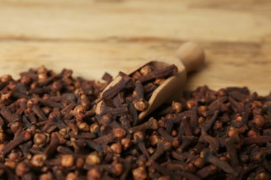 Photo of Aromatic dry cloves and wooden scoop on table, closeup