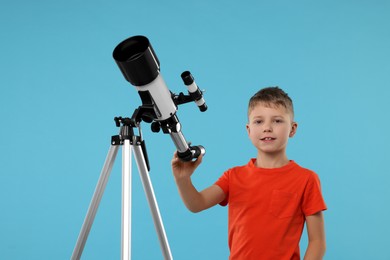 Photo of Cute little boy with telescope on light blue background