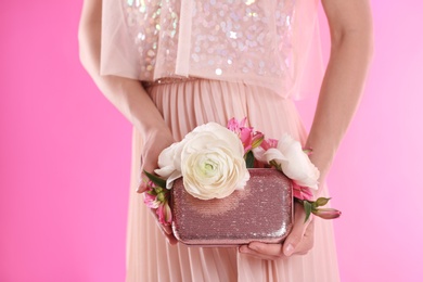 Photo of Woman holding elegant handbag with spring flowers on pink background, closeup