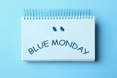 Notebook with text Blue Monday on color background, top view