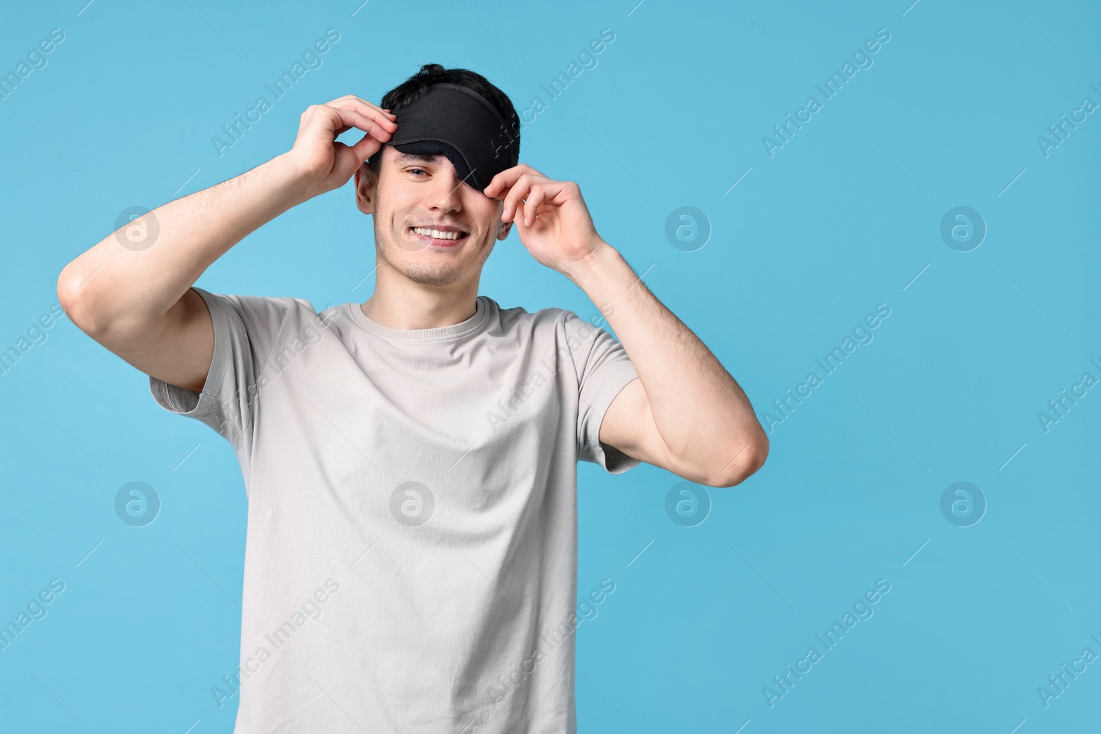 Photo of Happy man in pyjama and sleep mask on light blue background, space for text