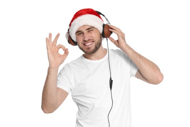 Young man in Santa hat listening to Christmas music on white background