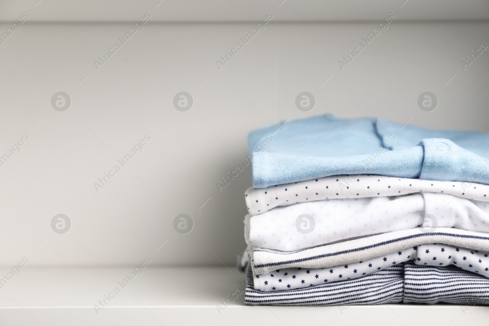 Photo of Stacked baby clothes on shelf. Space for text