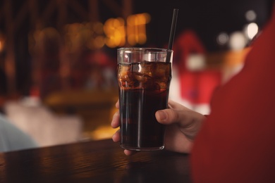 Man holding glass of refreshing cola at table indoors, closeup. Space for text