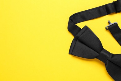 Photo of Stylish black bow tie on yellow background, top view. Space for text