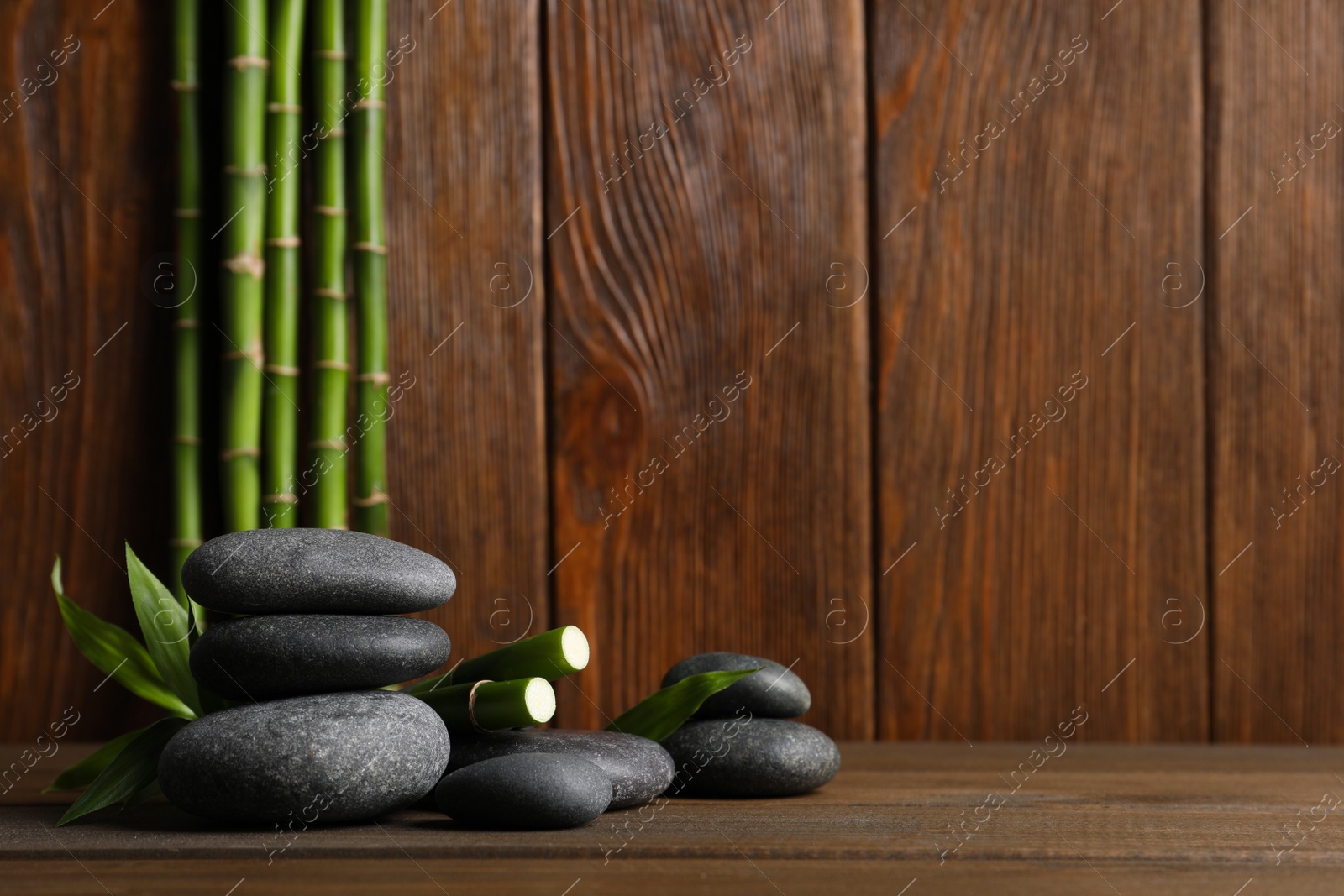Photo of Spa stones and bamboo stems on wooden table. Space for text