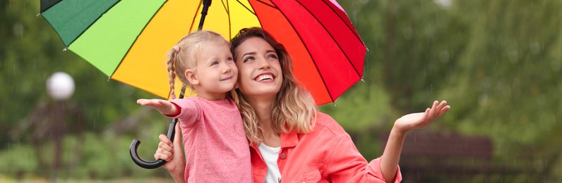 Image of Happy mother and daughter with bright umbrella under autumn rain outdoors. Banner design