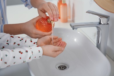 Mother and daughter washing hands with liquid soap in bathroom, closeup