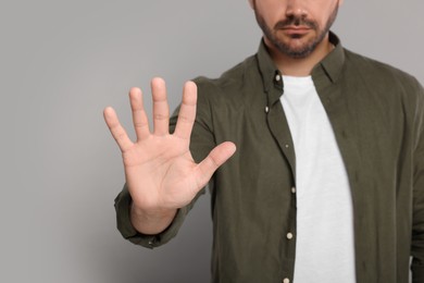 Man showing stop gesture on light grey background, closeup