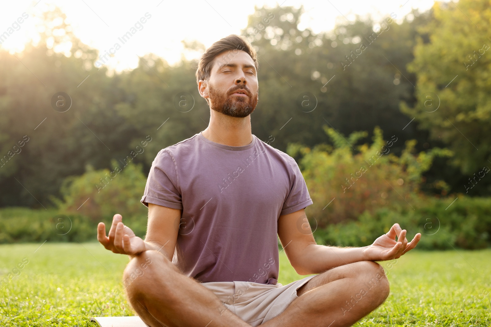 Photo of Man practicing yoga on mat outdoors. Lotus pose