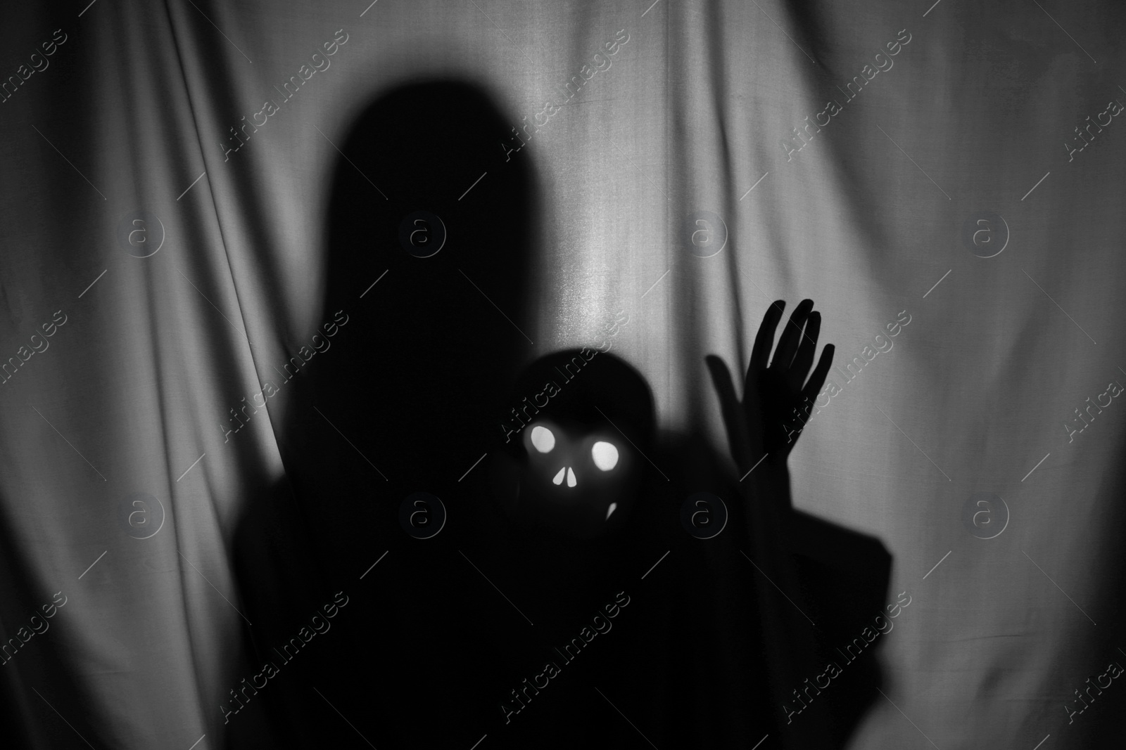 Photo of Silhouette of creepy ghost with skull behind grey cloth