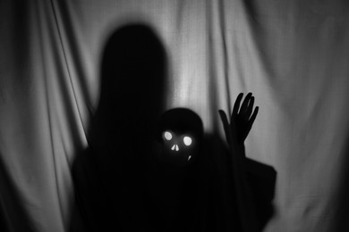 Photo of Silhouette of creepy ghost with skull behind grey cloth