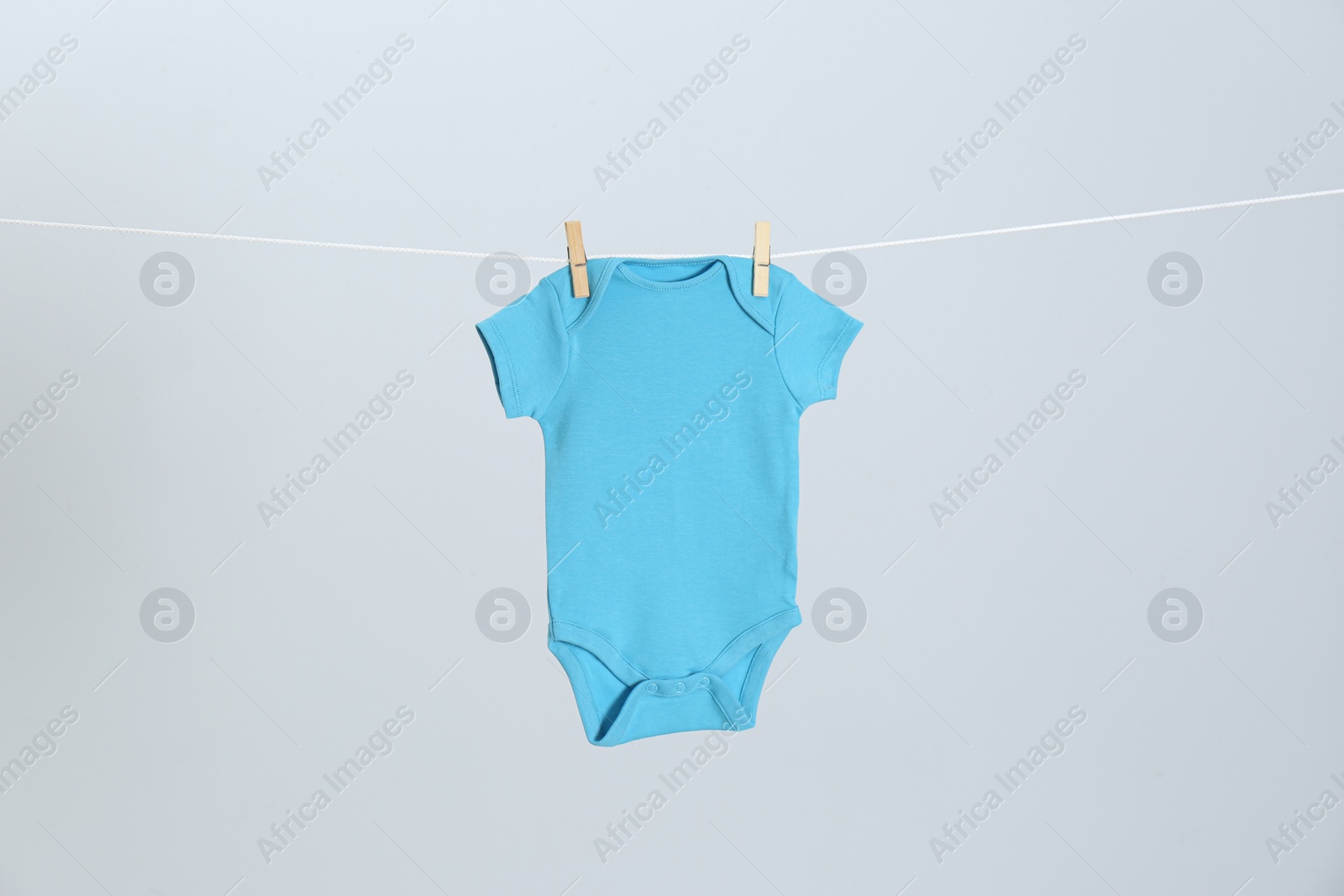 Photo of Cute baby onesie hanging on clothes line against light grey background. Laundry day