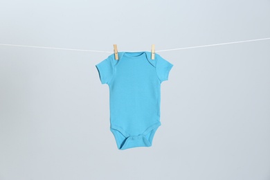 Photo of Cute baby onesie hanging on clothes line against light grey background. Laundry day