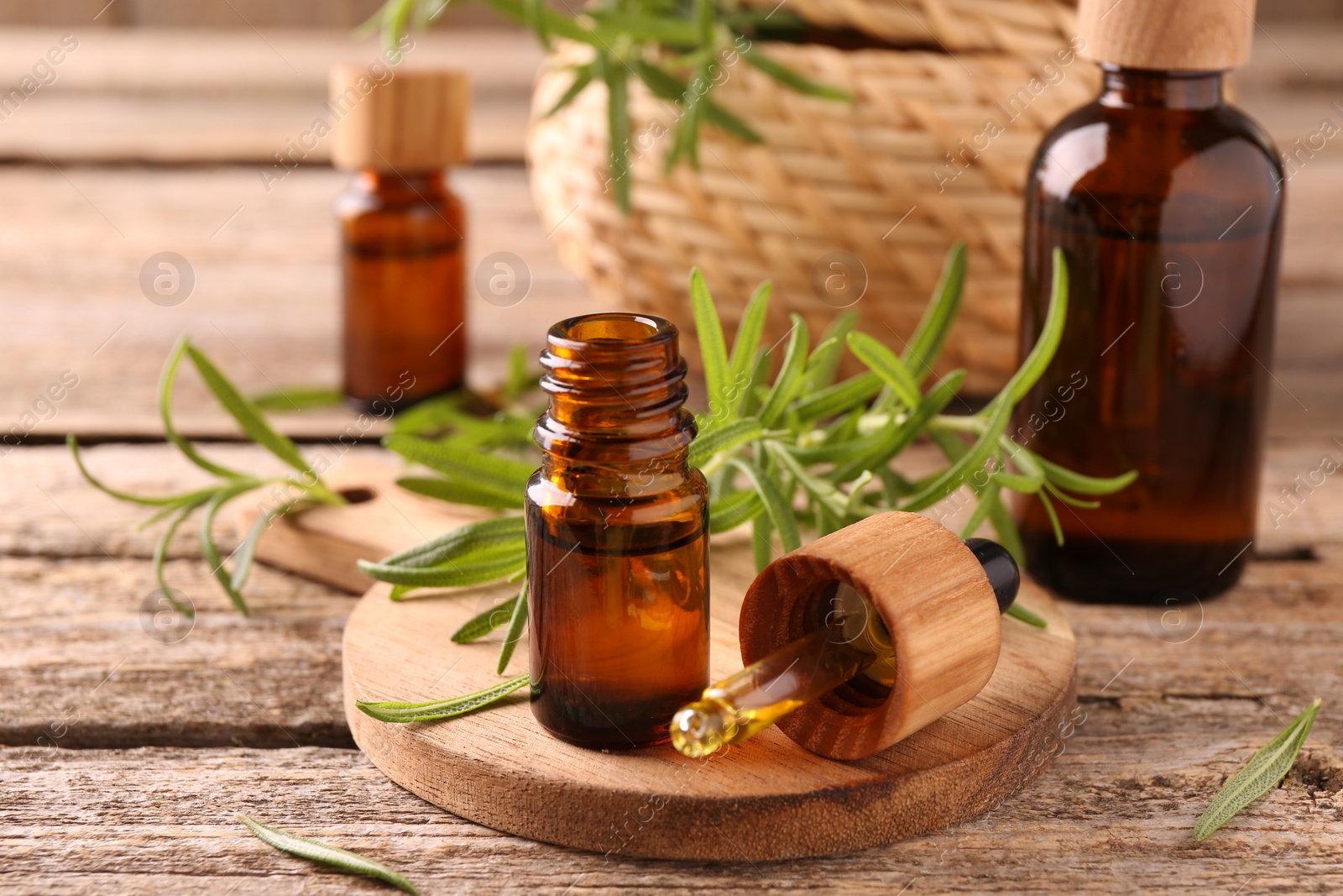 Photo of Aromatic essential oils in bottles, pipette and rosemary on wooden table, closeup