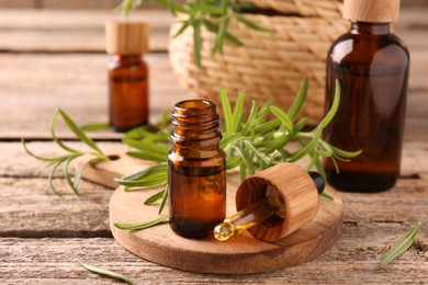 Photo of Aromatic essential oils in bottles, pipette and rosemary on wooden table, closeup