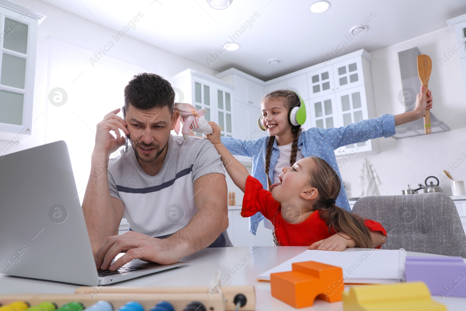 Photo of Children disturbing stressed man in kitchen. Working from home during quarantine