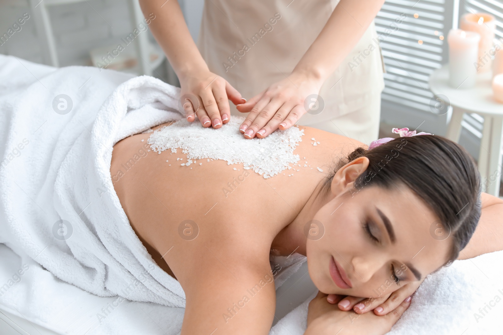 Photo of Young woman having body scrubbing procedure with sea salt in spa salon