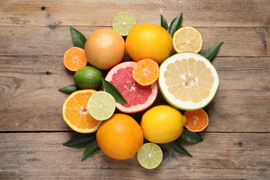 Photo of Different ripe citrus fruits with green leaves on wooden table, flat lay