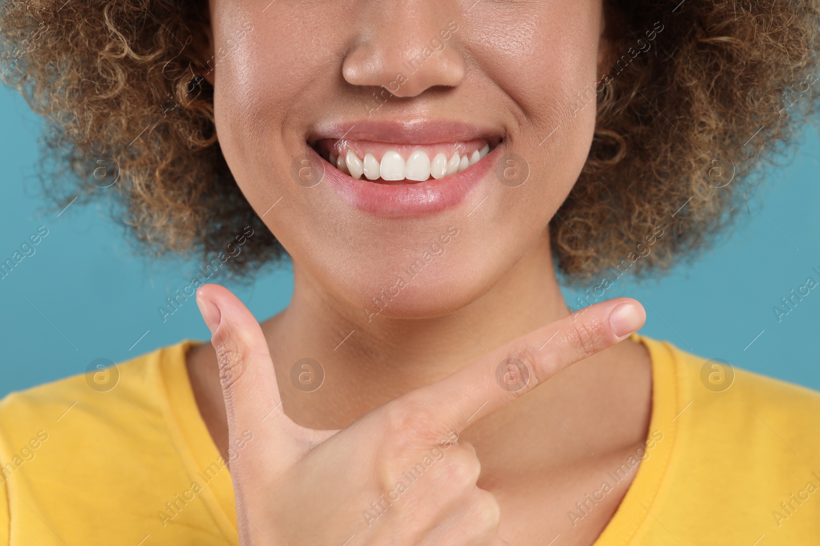 Photo of Woman showing her clean teeth and smiling on light blue background, closeup