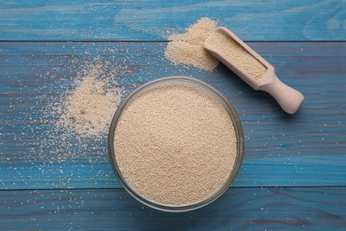 Bowl and scoop with active dry yeast on light blue wooden table, flat lay