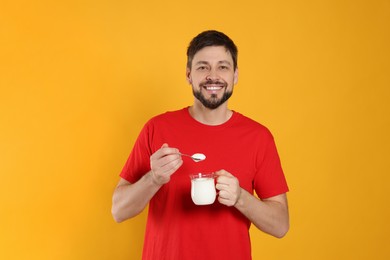 Handsome man with tasty yogurt on orange background