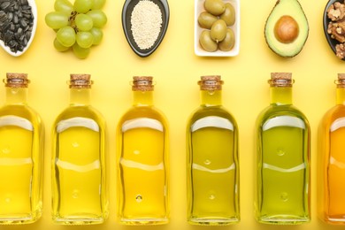 Vegetable fats. Different oils in glass bottles and ingredients on yellow table, flat lay