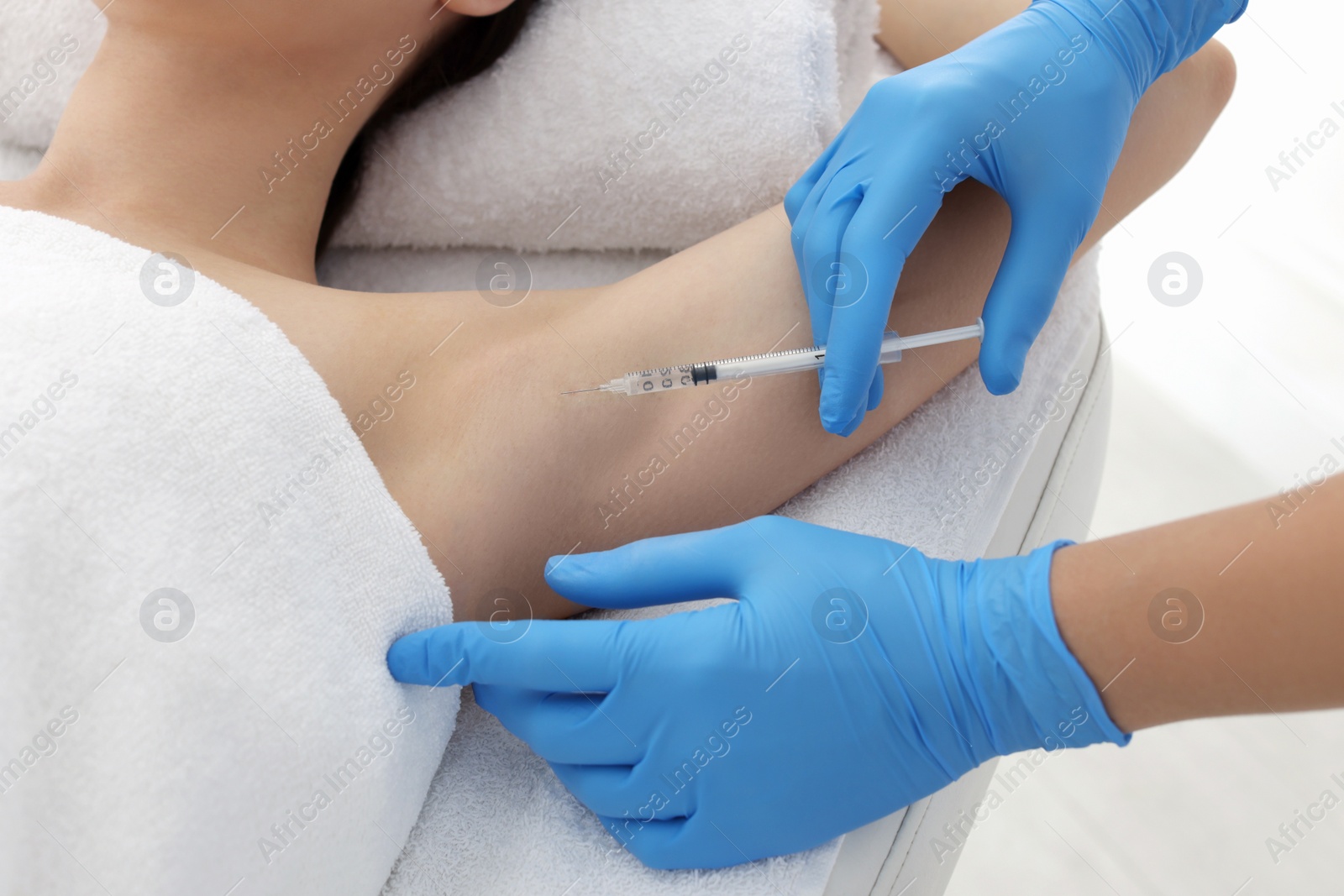 Photo of Cosmetologist injecting young woman's armpit in clinic, closeup. Treatment of hyperhidrosis