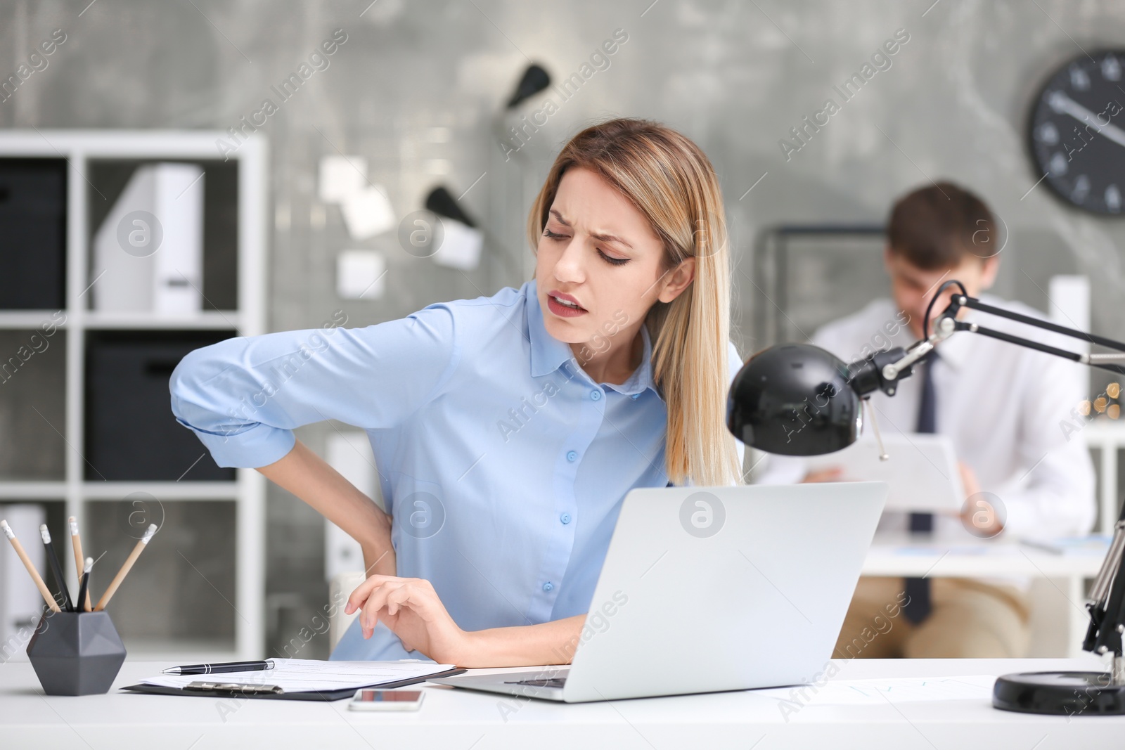 Photo of Young woman suffering from back pain in office