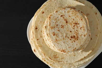 Many tasty homemade tortillas on black wooden table, top view