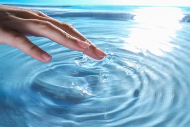 Woman touching clear water, closeup. Making ripples