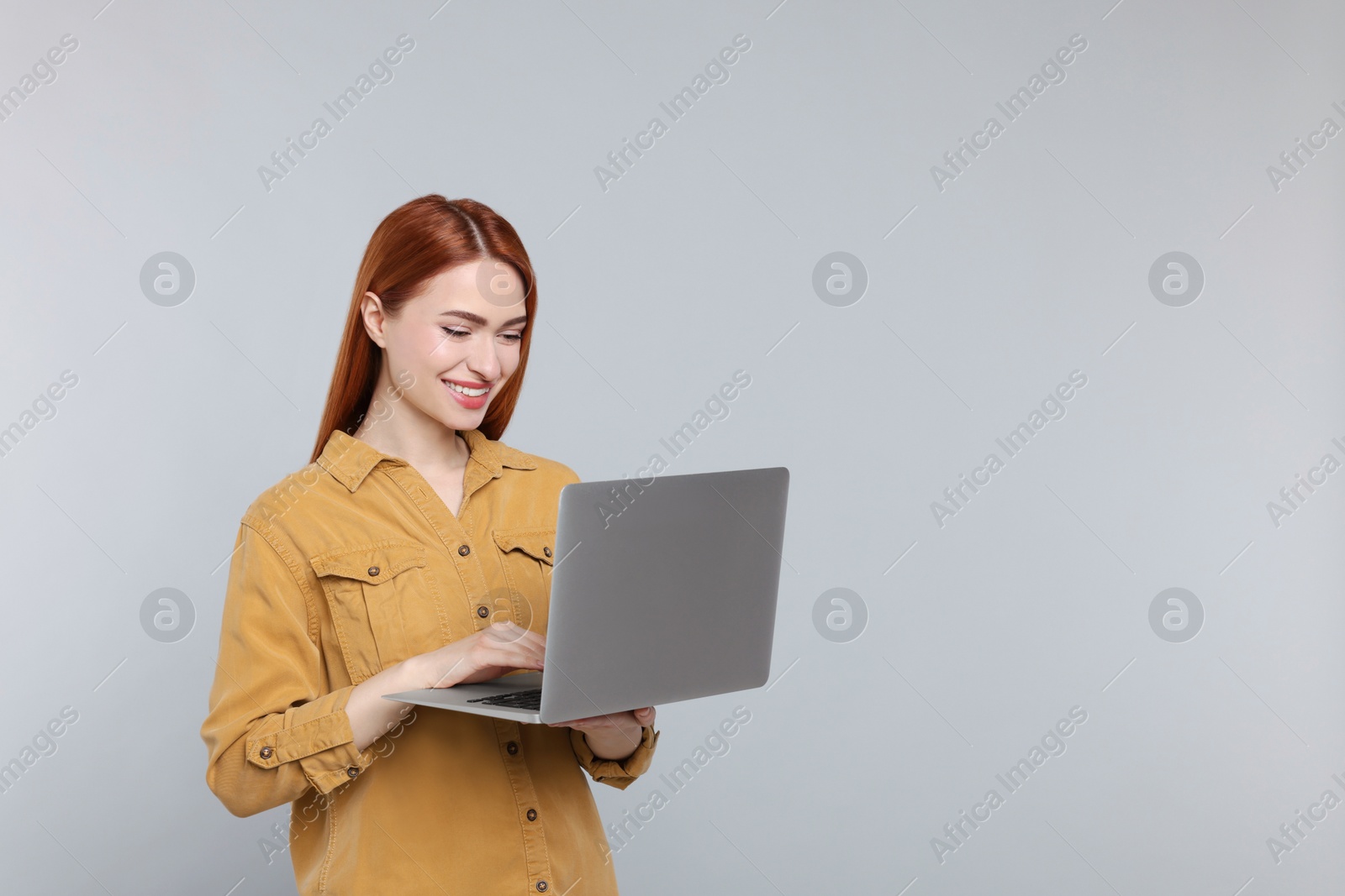 Photo of Smiling young woman working with laptop on grey background, space for text