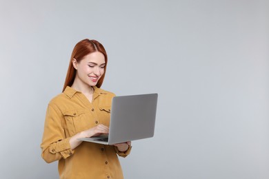 Smiling young woman working with laptop on grey background, space for text
