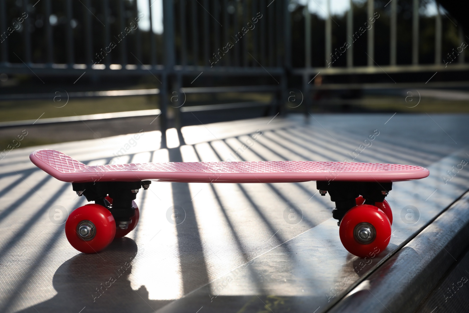 Photo of Modern pink skateboard with red wheels on top of ramp outdoors