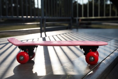 Modern pink skateboard with red wheels on top of ramp outdoors