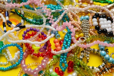 Photo of Pile of beautiful handmade beaded jewelry on yellow background, closeup