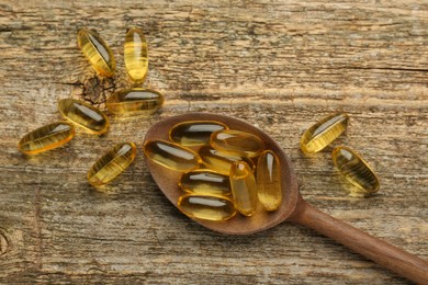 Photo of Vitamin capsules in spoon on wooden table, top view