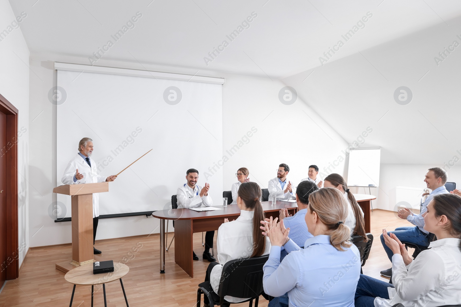 Photo of Senior doctor giving lecture in conference room with projection screen