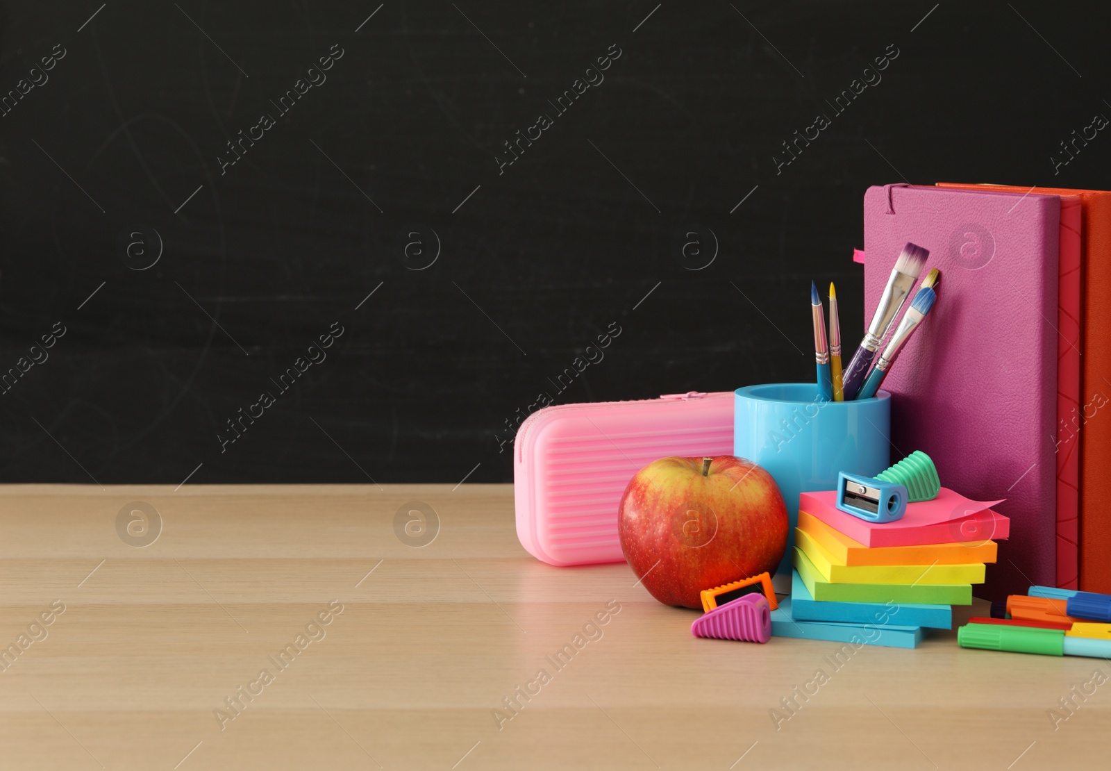 Photo of Different school stationery on wooden table near blackboard, space for text. Back to school