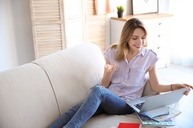 Young blogger with laptop sitting on sofa at home