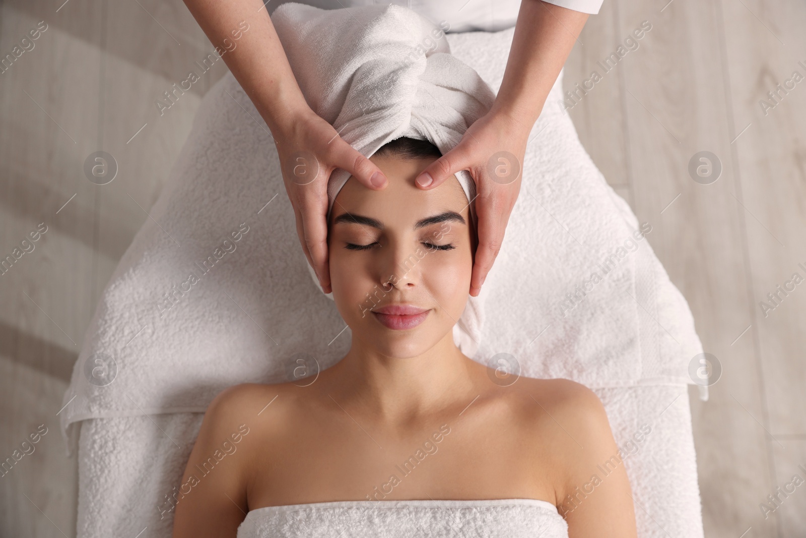 Photo of Beautiful woman receiving facial massage in beauty salon, closeup. Top view