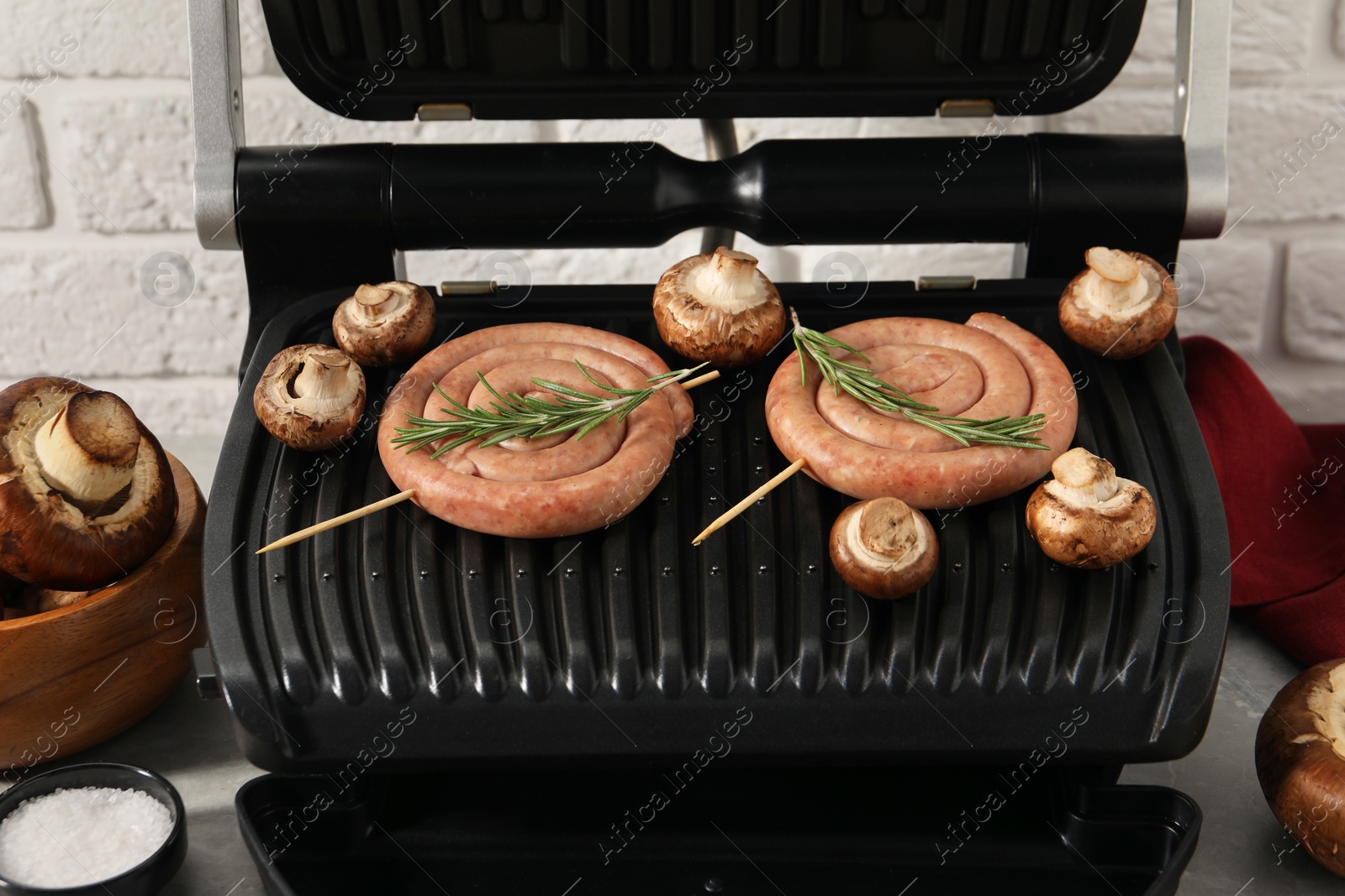 Photo of Electric grill with homemade sausages, rosemary and mushrooms on table