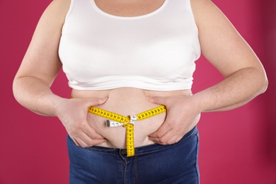 Photo of Overweight woman measuring waist with tape on color background, closeup